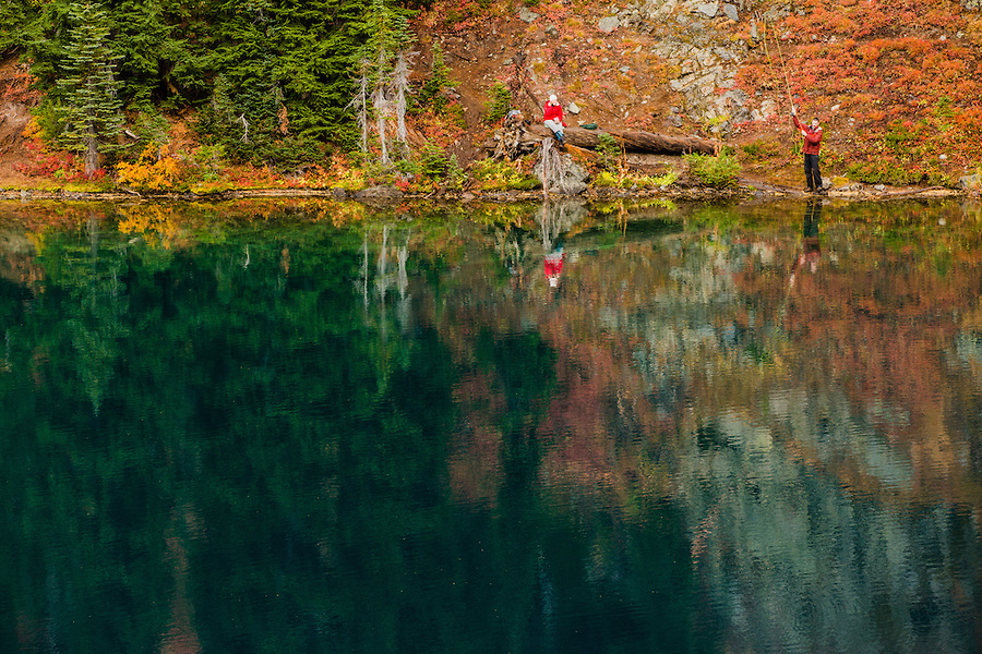 An woman sits and eats a snack while her male companion is engaged in fly fishing in Blue Lake in Washington's North Cascade Mountains.